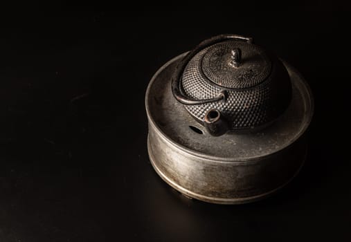 Bangkok, Thailand - 17 Sep, 2024 - Black cast iron kettle or teapot on Iron tray for kettle with black background. Light and Shadow, Space for text, Selective Focus.