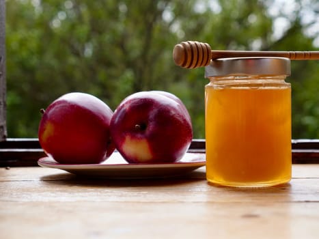 Apples red whole and sliced with a jar of honey on the traditional Jewish holiday of Rosh Hashana on a wooden table by the window on a sunny day. Close-up