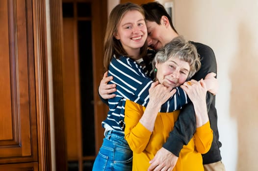 Young boy and a girl happily hug their grandmother, the family lovingly takes care of their elderly parents and congratulates them on the holiday, the grandson with his sister visit an elderly woman.