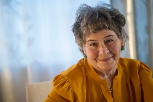 A portrait of a laughing, smiling elderly woman with gray hair and wrinkles on her face, but young at heart and leading an active lifestyle. Happy pensioner is pretty posing in her cozy home.