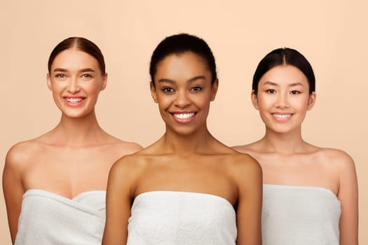 Three Attractive Women In Bath Towels Smiling At Camera Posing In Studio Over White Background. Body Care And Beauty