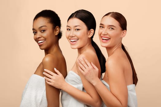 Beauty And Skincare. Three Mixed Model Girls In Bath Towels Posing Smiling To Camera Over White Studio Background