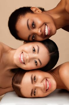 Three Diverse Girls With Perfect Faces And Skin Posing Together Smiling To Camera On Gray Background. Multicultural Beauty Concept. Vertical