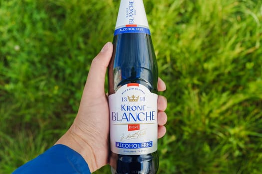 Tyumen, Russia-August 10, 2024: hand grasps a chilled bottle of alcohol-free Krone Blanche while sitting on a swing in a sunny park