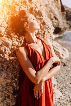 Woman red dress sea. Woman in a long red dress posing on a beach with rocks on sunny day. Girl on the nature on blue sky background