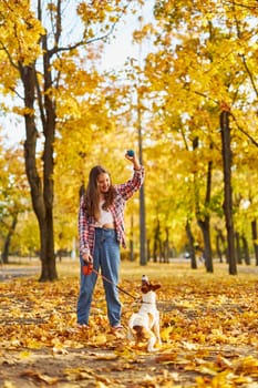 Happy joyful little girl playing with her funny Jack Russell Terrier in beautiful autumn forest, child playing and having fun with dog during walk in nature. Children and pets outdoors