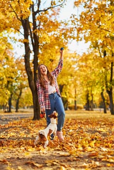Happy joyful little girl playing with her funny Jack Russell Terrier in beautiful autumn forest, child playing and having fun with dog during walk in nature. Children and pets outdoors