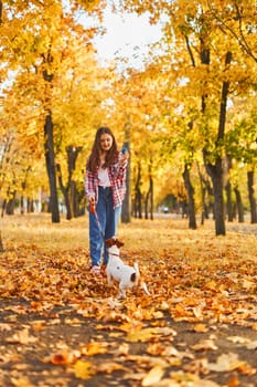 Happy joyful little girl playing with her funny Jack Russell Terrier in beautiful autumn forest, child playing and having fun with dog during walk in nature. Children and pets outdoors