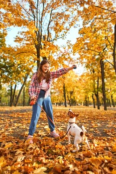 Happy joyful little girl playing with her funny Jack Russell Terrier in beautiful autumn forest, child playing and having fun with dog during walk in nature. Children and pets outdoors