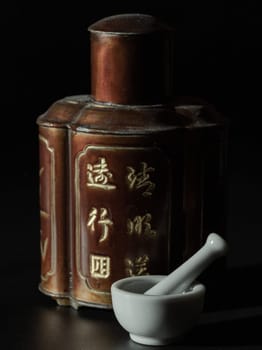 Bangkok, Thailand - 18 Sep, 2024 - Small white mortar and pestle made of porcelain or ceramic (used for grinding medicinal tablets, spices) in front of Antique chinese tea leaf iron storage jar (Translation meaning chinese characther is the name of the tea). Traditional chinaese metal canister, Copy space, Selective focus.