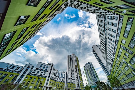 The picture shows a group of modern apartment buildings photographed from a low angle, emphasizing their height against a cloudy sky