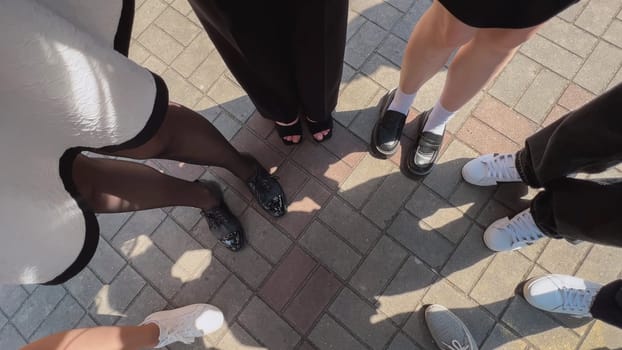 Group of people are standing on a pavement, their feet and shoes visible from above