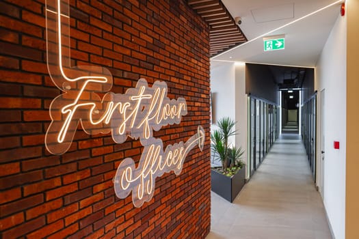 A brick wall stands prominently with a vibrant neon sign affixed to it, casting a bold glow against the rugged texture of the bricks. The neon sign illuminates the area with its bright colors, creating a striking contrast against the dull backdrop of the wall.