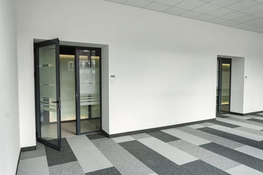 Office space devoid of furniture or decoration, containing only two doors and a black-and-white checkered floor. The doors are closed, leading to unknown destinations, while the floor adds a geometric pattern to the space.