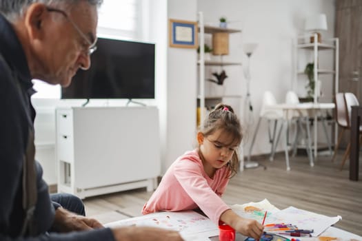 A young girl colors while her grandfather watches with pride.