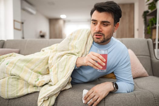 A man is seen sitting comfortably on a couch, holding a drink in his hand. He appears relaxed and content as he enjoys his beverage.