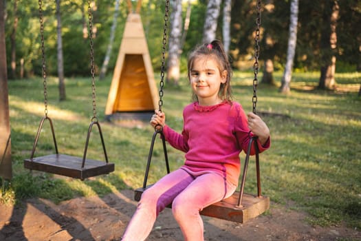 Cute smiling girl on a swing in the playground.
