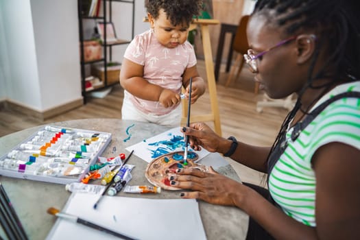 A young child curiously explores painting while seated beside a parent.