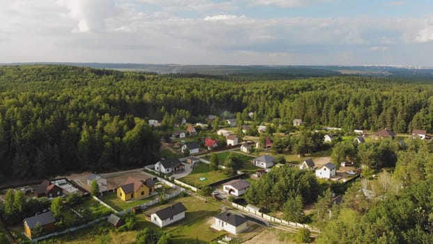 Aerial perspective of a forest surrounded residential area with new detached houses boasting green lawns and fences