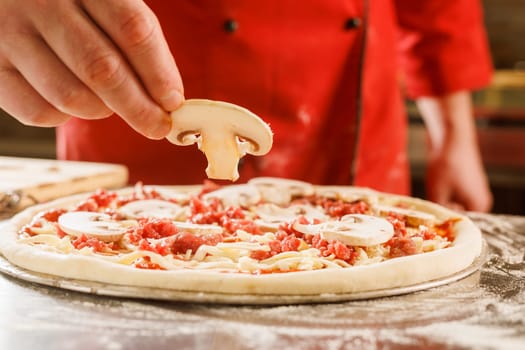 Chef adding mushroom slices to an uncooked pizza with tomato sauce, cheese, and ground meat.