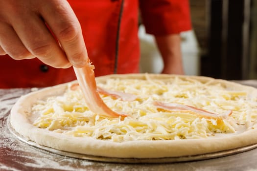 Close-up of a chef adding bacon to a cheese pizza before baking.