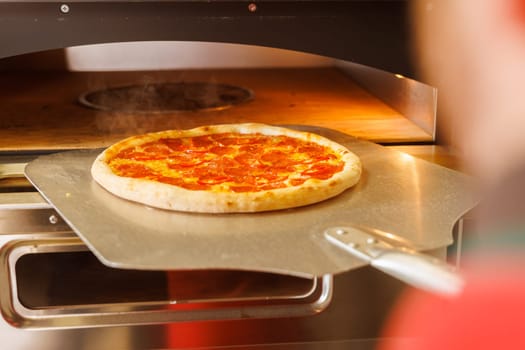 A freshly baked pizza being taken out of a pizza oven using a pizza peel.
