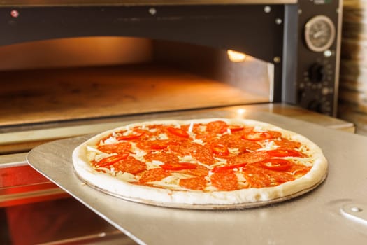 A freshly baked pizza being taken out of a pizza oven using a pizza peel.