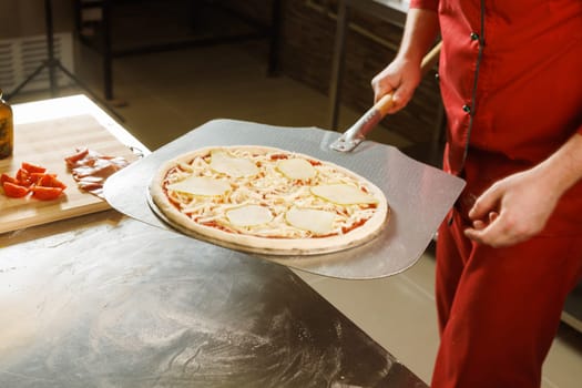 A chef in a red uniform prepares to place a pizza with cheese and tomato slices into an oven.