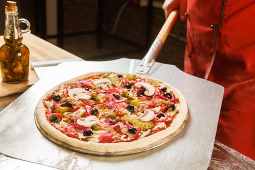 A chef in a red uniform prepares to place a pizza with cheese and tomato slices into an oven.