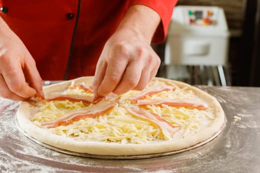 Close-up of a chef adding bacon to a cheese pizza before baking.