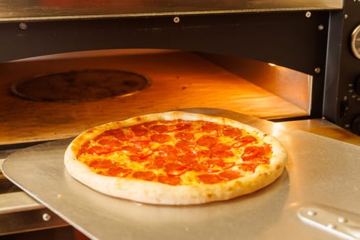 A freshly baked pizza being taken out of a pizza oven using a pizza peel.