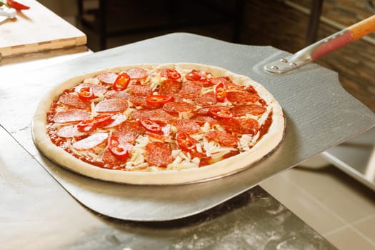 A chef in a red uniform prepares to place a pizza with cheese and tomato slices into an oven.