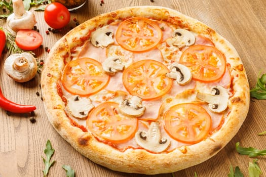 A freshly baked pizza topped with sliced tomatoes and mushrooms on a wooden table.