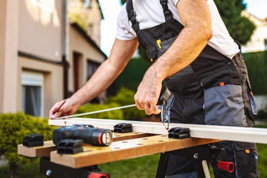Unrecognizable male carpenter measuring wooden plank outdoors.