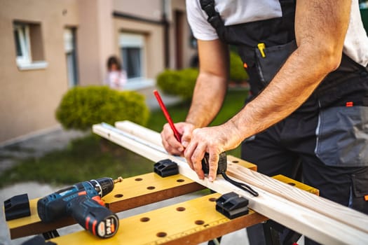 Unrecognizable men measuring wooden plank outdoors.