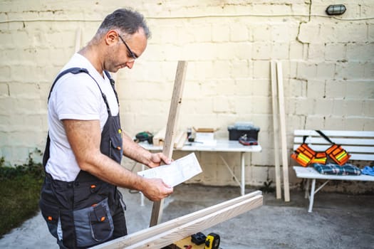 Mature male carpenter working with wooden plank outdoors.