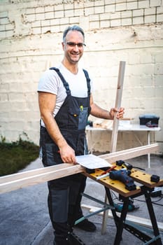 Mature male carpenter working with wooden plank outdoors.
