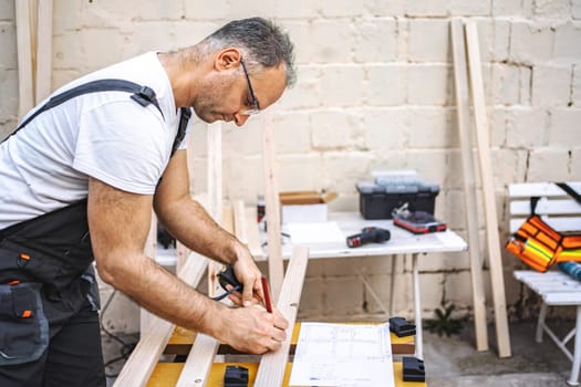 Mature male carpenter measuring wooden plank outdoors.