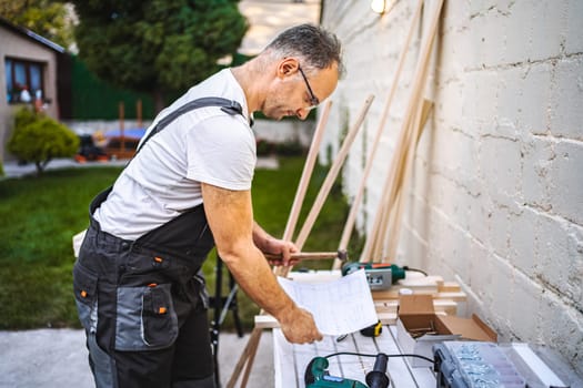 Mature male carpenter working with wooden plank outdoors.