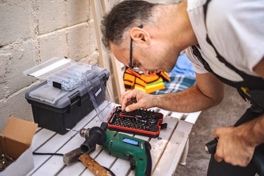 Mature male carpenter using electric screwdriver on a wooden plank outdoors.