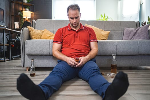 Drunk man sitting on the floor while drinking alcohol.