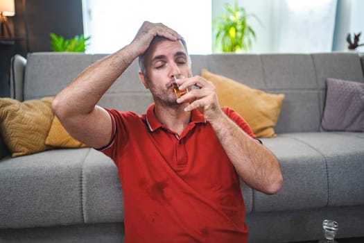 Mature man sitting on the floor and drinking alcohol.