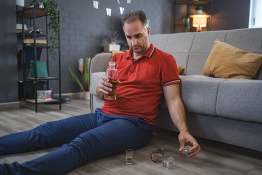 Mature man sitting on the floor and drinking alcohol.