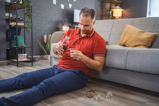 Mature man sitting on the floor and drinking alcohol.