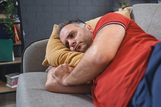 Man alone at home lying on sofa looking sad and distraught.