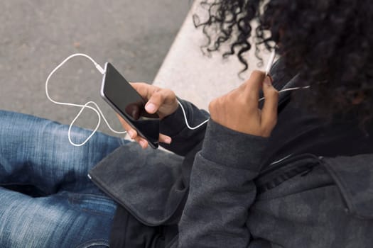 unrecognizable teenager listening to music on his mobile phone, concept of technology of communication and urban lifestyle