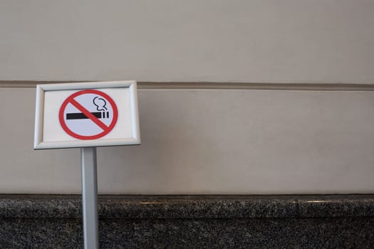 Sign prohibiting smoking on special pole near building, no smoking area against the background of wall