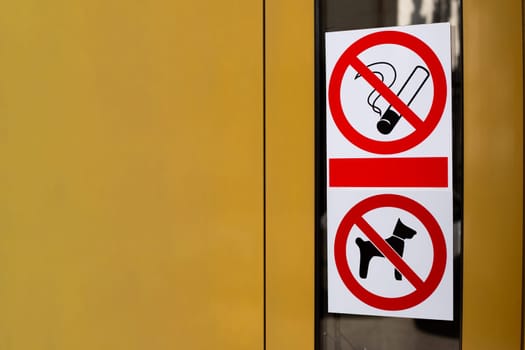 Signs prohibiting smoking and entry into building with dogs. Restricted area with no access for pets. Crossed out cigarette and dog on sticker on building door