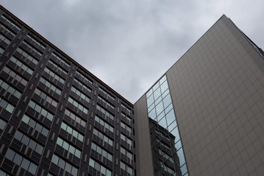 Photo from bottom to top view of corners of office buildings and gray gloomy sky on cloudy day, atmospheric photo of the working environment of office businessmen