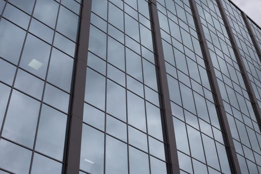 Glass facade of building goes up into the gray gloomy sky, cloudy sad day for routine work in office